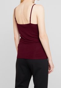 Top marsala senza maniche con spalline regolabili sottili, design aderente, texture morbida e orlo rifinito, abbinato a pantaloni neri.