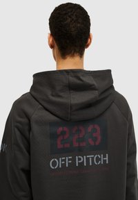 Ciemnoszara bluza z kapturem z dużą grafiką na plecach z napisem "223" w burgundzie i "OFF PITCH" w bieli; gładka tekstura o dopasowanym kroju.