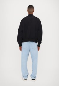 Black bomber jacket with ribbed cuffs and hem, paired with light blue loose-fit jeans. The look is completed with white and black sneakers.