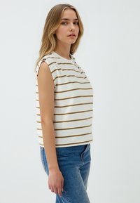 Blusa senza maniche color crema con sottili righe orizzontali marroni. Presenta un colletto rotondo, una vestibilità morbida e bottoni sugli accenti delle spalle.