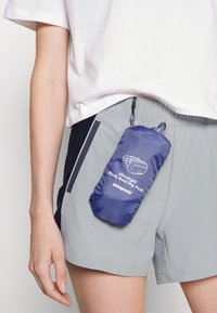 Ultralätt höftväska i marinblått, nedpackad i sig själv. Har ett slitstarkt tyg, dragsko och vittryckt logo på framsidan.