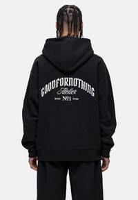 Felpa nera oversize con grafica bianca sul retro. Realizzata in tessuto morbido, con cappuccio e polsini a coste.