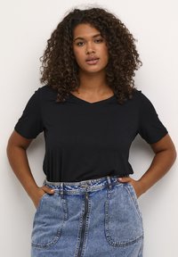 Black short-sleeve t-shirt with a v-neckline, paired with a blue denim skirt featuring a front zipper and large pockets.