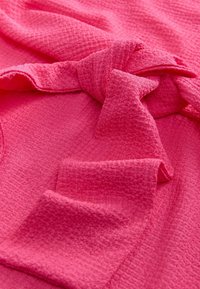 Gros plan d'un tissu texturé rose vif avec un grand nœud noué au centre et des plis doux autour.