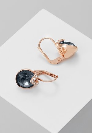 Náušnice na páčku z růžového zlata s velkými tmavě šedými broušenými kameny a malými čirými krystaly na bílém povrchu.