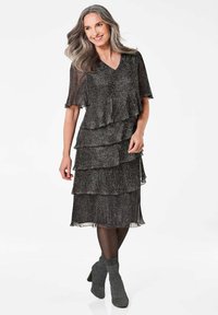 Schwarzes und silbernes, gestuftes Kleid mit V-Ausschnitt und kurzen Ärmeln. Strukturierter Stoff mit schimmerndem Finish. Kombiniert mit grauen Knöchelstiefeln.