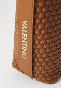 Vevd brun lær håndveske med en glatt stropp, som har en fremtredende gull "VALENTINO" logo på en teksturert panel.