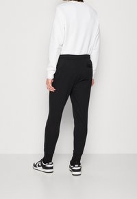 Svarta joggerbyxor med en smal passform, elastisk midja och en diskret bakficka, matchade med en vit sweatshirt och svarta sneakers.