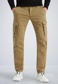 Pantalons cargo beiges avec plusieurs poches latérales, coupe droite, tissu en coton durables, et détails de couture visibles, associés à des baskets blanches.