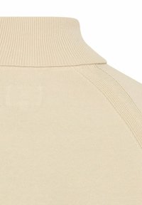 Beige gerippter Strickpullover mit Rollkragen, Nahaufnahme des Kragens und der Schulternahtnähte.