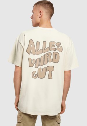 Cremefarvet bomulds t-shirt med et stort, lysebrunt boble-bogstav grafisk motiv på ryggen, der siger "ALLES WIRD GUT." Løs pasform, korte ærmer.