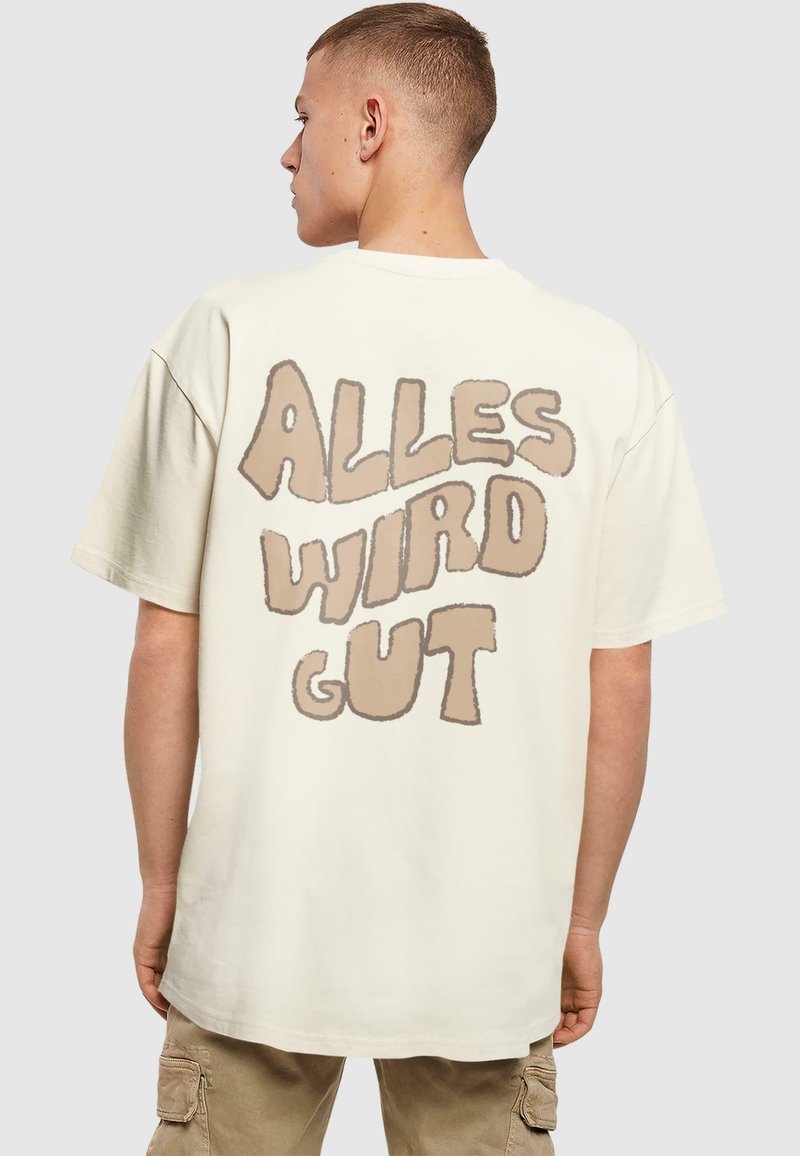 Krämfärgad bomull t-shirt med en stor, ljusbrun bubbelfärgad grafisk text på baksidan som säger "ALLES WIRD GUT." Avslappnad passform, kort ärm.