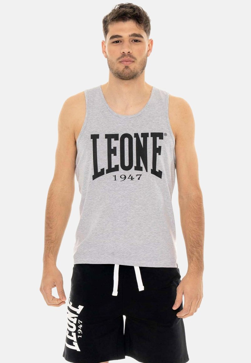 Homme portant un débardeur gris et un short noir, tous deux imprimés « LEONE 1947 », debout devant un fond uni clair.