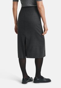 Jupe crayon à carreaux gris avec une fente au dos, réalisée en tissu texturé. Portée avec des collants noirs et des mocassins, mettant en valeur une coupe ajustée.