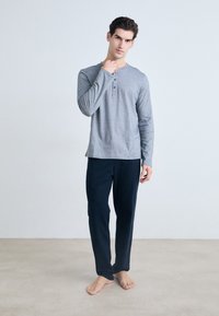 Camisa henley de manga larga gris con tres botones, combinada con pantalones de lounge azul marino, hechos de una tela suave, adecuados para el uso casual.