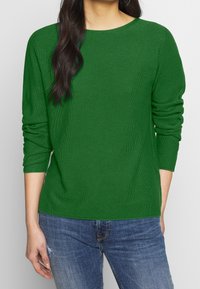 Green knit sweater with a round neckline and three-quarter sleeves, featuring a soft texture. Paired with blue denim jeans.