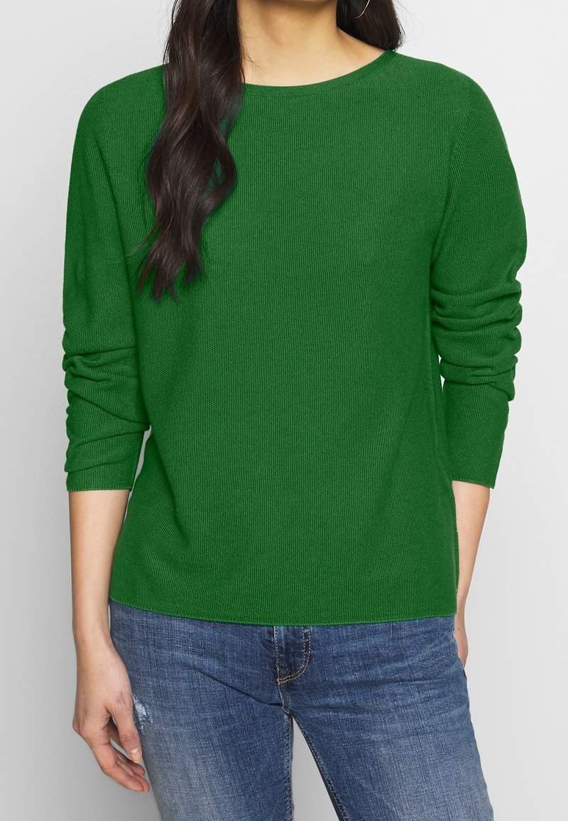 Green knit sweater with a round neckline and three-quarter sleeves, featuring a soft texture. Paired with blue denim jeans.