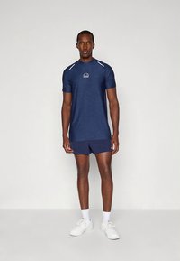 Öösinine spordipluus lühikeste varrukatega ja rinnal logoga, sobitatud sama värvi lühikeste pükstega. Materjal näib kerge ja hingav.