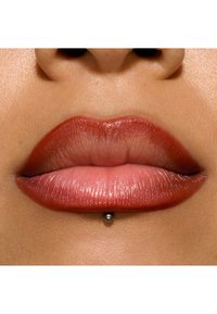 Close-up of full lips with a glossy red-brown finish, featuring a silver ball accessory centered below the lower lip and smooth skin texture.