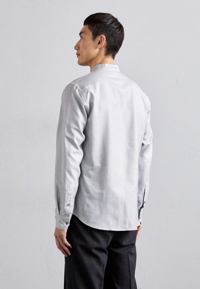 Camisa gris texturizada de manga larga con cuello mao, puños abotonados y un patrón sutil, combinada con pantalones oscuros.