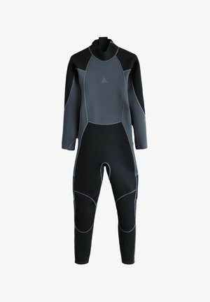 Junger männlicher Surfer in schwarzem Neoprenanzug, der barfuß am Strand entlanggeht und ein türkisfarbenes Surfbrett nahe den Wellen hält.