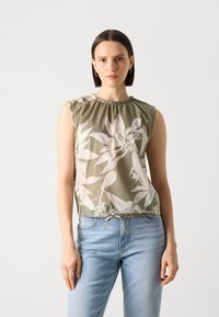Grön blommig ärmlös topp med samlad halsringning och dragsko i nederkant, tillverkad av lättviktsmaterial. Bärs med ljusblå jeans.