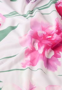 Blomsterstof med store rosa og lilla blomster på en hvid baggrund, med grønne blade og subtile stribede detaljer. Tekstureret overflade.