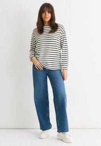 Black and white striped sweater with long sleeves, paired with wide-leg blue denim jeans, and white sneakers on a plain background.