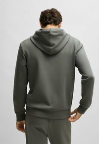 Felpa con cappuccio di colore verde oliva, realizzata in materiale morbido. Presenta polsini e orlo a costine, con una texture liscia e una vestibilità comoda.