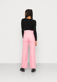 Calças largas de cintura alta em rosa, com uma textura suave e dois bolsos traseiros, combinadas com uma blusa preta de manga longa ajustada.