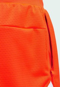 Oranžové síťované atletické šortky s prodyšným materiálem, bočním zipovým kapsou a hladkým vnitřním podšívkou. Viditelný horizontální šev.