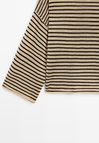 Tissu tricoté rayé horizontalement beige et noir montrant une manche longue et une partie du torse d'un vêtement.