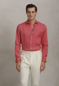 Camisa de linho vermelha com um corte ajustado, com botões, combinada com calças em crème com pregas e um laço lateral.