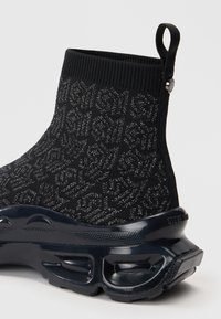Czarne wysokie sneakersy z dzianiny o teksturowanym wzorze, z grubą wyściełaną podeszwą i pętelką na pięcie z metalowym detalem.