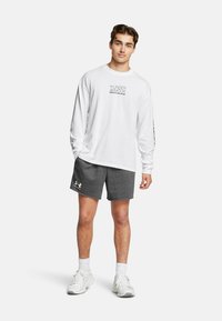 Vit långärmad skjorta med svart text, tillsammans med grå träningsshorts. Skjortan har en logotyp och tryck på ärmarna. Vita skor.