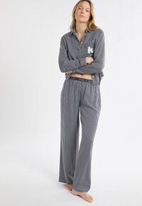 Komplet piżamowy w paski w kolorze ciemnoniebieskim i białym, składający się z koszuli zapinanej na guziki z kieszonką oraz szerokich spodni z elastycznym pasem.