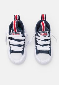 Navy plátěné vysoké tenisky s bílými gumovými podrážkami, bílými tkaničkami a červenými, bílými a modrými proužkovanými poutky na patě. Viditelné logo Converse All Star.