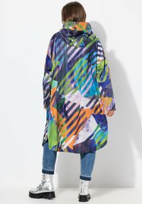 Giacca impermeabile colorata e con motivo, dotata di cappuccio. Presenta disegni geometrici in viola, blu, verde e arancione, realizzata in un materiale leggero.