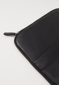 Sort læder laptop sleeve med lynlås, der har en tekstureret overflade, glatte accenter og en lille lædertrækflap.