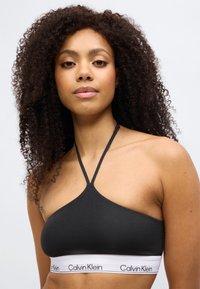 Μαύρο κοντοκομμένο σουτιέν bralette με σχέδιο ψηλού λαιμού, ομαλή υφή και λευκή ελαστική ταινία με τη στάμπα "Calvin Klein".