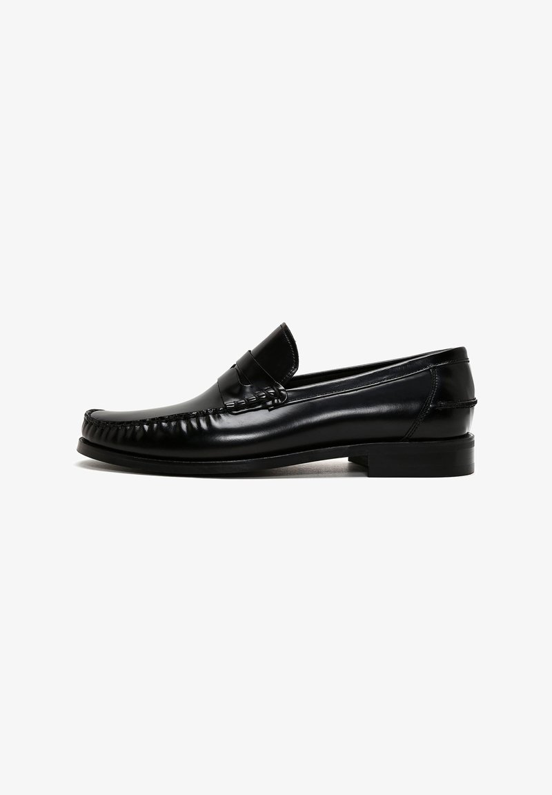 Mocassins en cuir noir avec un bout rond, des détails cousus le long des bords et un petit talon carré. Texture lisse et design minimaliste.