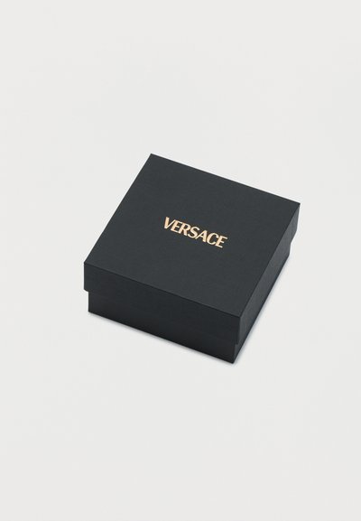 Μαύρο τετράγωνο κουτί με χρυσό λογότυπο "VERSACE" στο κέντρο του καπακιού, τοποθετημένο σε απλό λευκό φόντο.