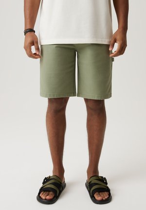 Oliwkowe szorty wykonane z miękkiego materiału; średniej długości o prostym kroju, z bocznymi kieszeniami i minimalnymi detalami w szyciu.
