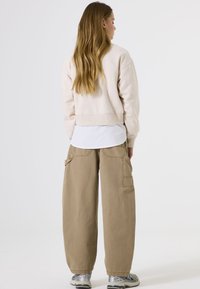 Beige cropped sweatshirt, gelaagd over een wit shirt, gecombineerd met losse beige cargo pants met zakken en opgerolde manchetten. Zilveren sneakers.