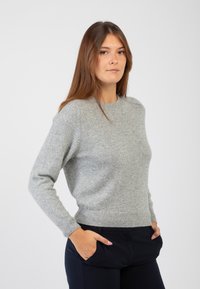 Maglione grigio chiaro lavorato a maglia con scollatura rotonda, maniche lunghe e orlo a coste. Texture morbida, design aderente, abbinato a pantaloni scuri.