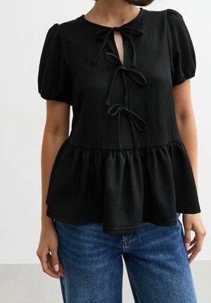 Zwarte textuur korte mouwen blouse met drie voorstrikken en een peplumzoom, gedragen met blauwe spijkerbroek bij een persoon.