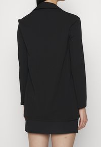 Černý blazer se strukturovaným designem, dlouhými rukávy a klopovým límcem. Hladká tkanina se dobře padnoucím střihem a minimálním detaily.