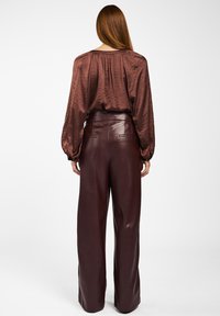 Langsleeve, brown satijnen blouse met geplooide achterkant, gecombineerd met high-waisted, bordeauxleren broek met platte zakken.