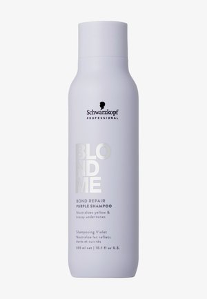 Witte plastic shampoofles met een slank ontwerp. Heeft een zwart logo en zilveren tekst. Het etiket geeft aan dat het gele en koperachtige tonen neutraliseert.