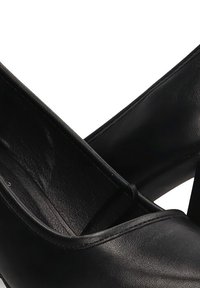 Zapatos de tacón alto de cuero negro con una textura suave, punta redondeada y una silueta clásica con sutiles detalles de costura.